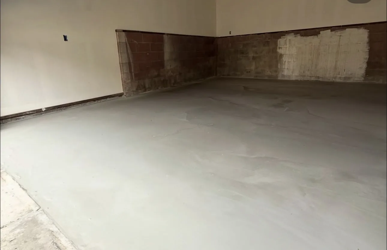 A garage floor part-way through, the pigmented base coat rolled out across the slab and still wet, the lower walls masked in a dark band, before any flake has been thrown into it