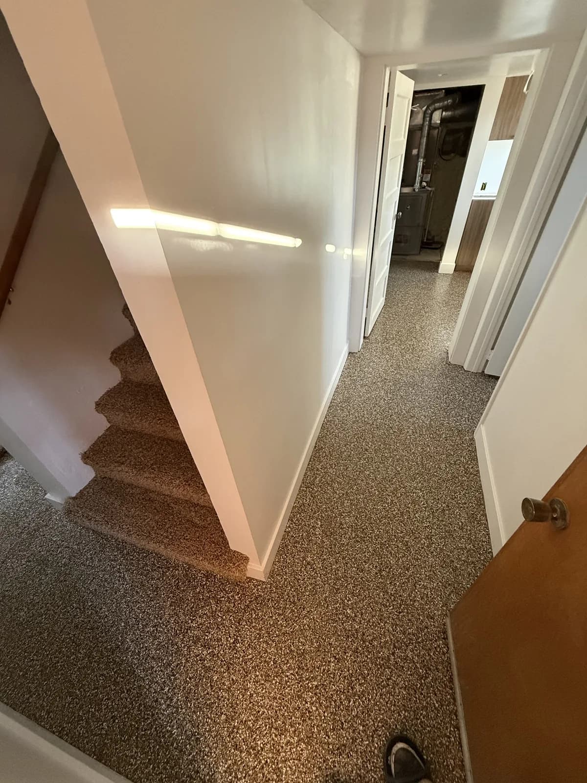 A tan flake floor at the foot of a carpeted staircase, the coating running to the bottom tread and on into a hallway
