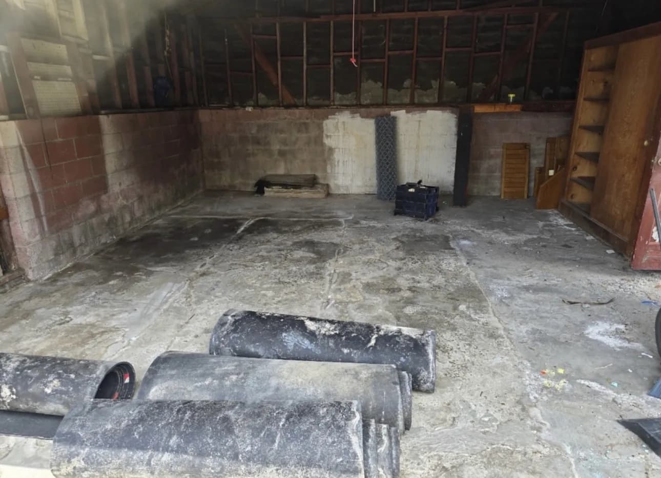The same block-walled space from another angle, its concrete floor stained and uneven, with lengths of pipe and timber lying across it