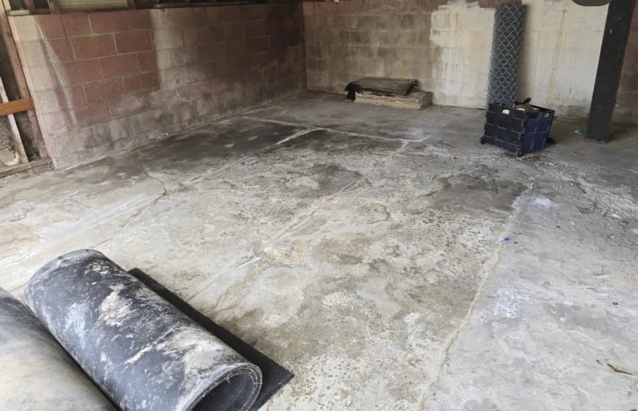 An old, stained and pitted concrete floor in a room with painted block walls, a roll of material and loose debris left on it