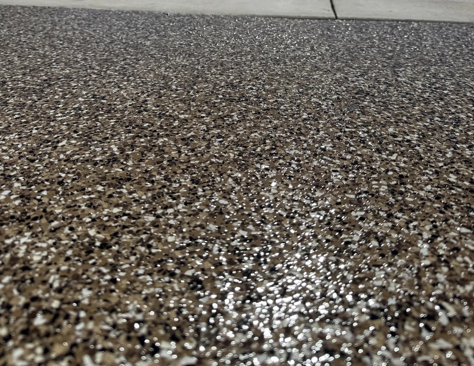A coated apron in tan, black and white flake photographed from ground level, meeting a plain concrete sidewalk at the top of the frame