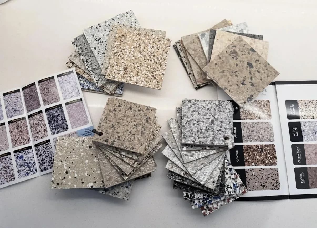 Dozens of square flake color samples and two bound sample decks fanned out on a white table, showing blends from pale greys and tans through to blue and black
