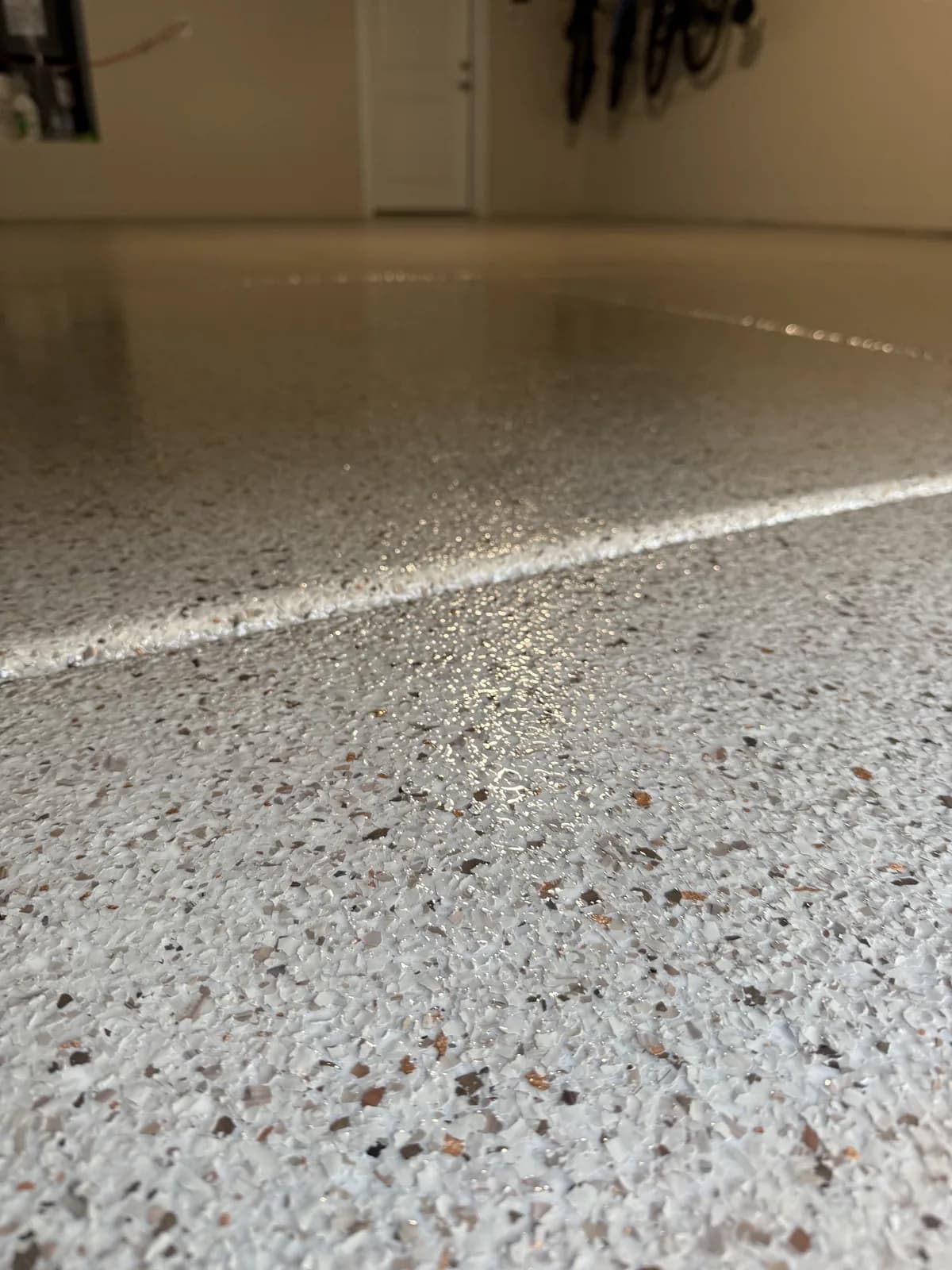 A low close view along a tan and white flake floor, a band of reflected light running across it, with a doorway out of focus beyond