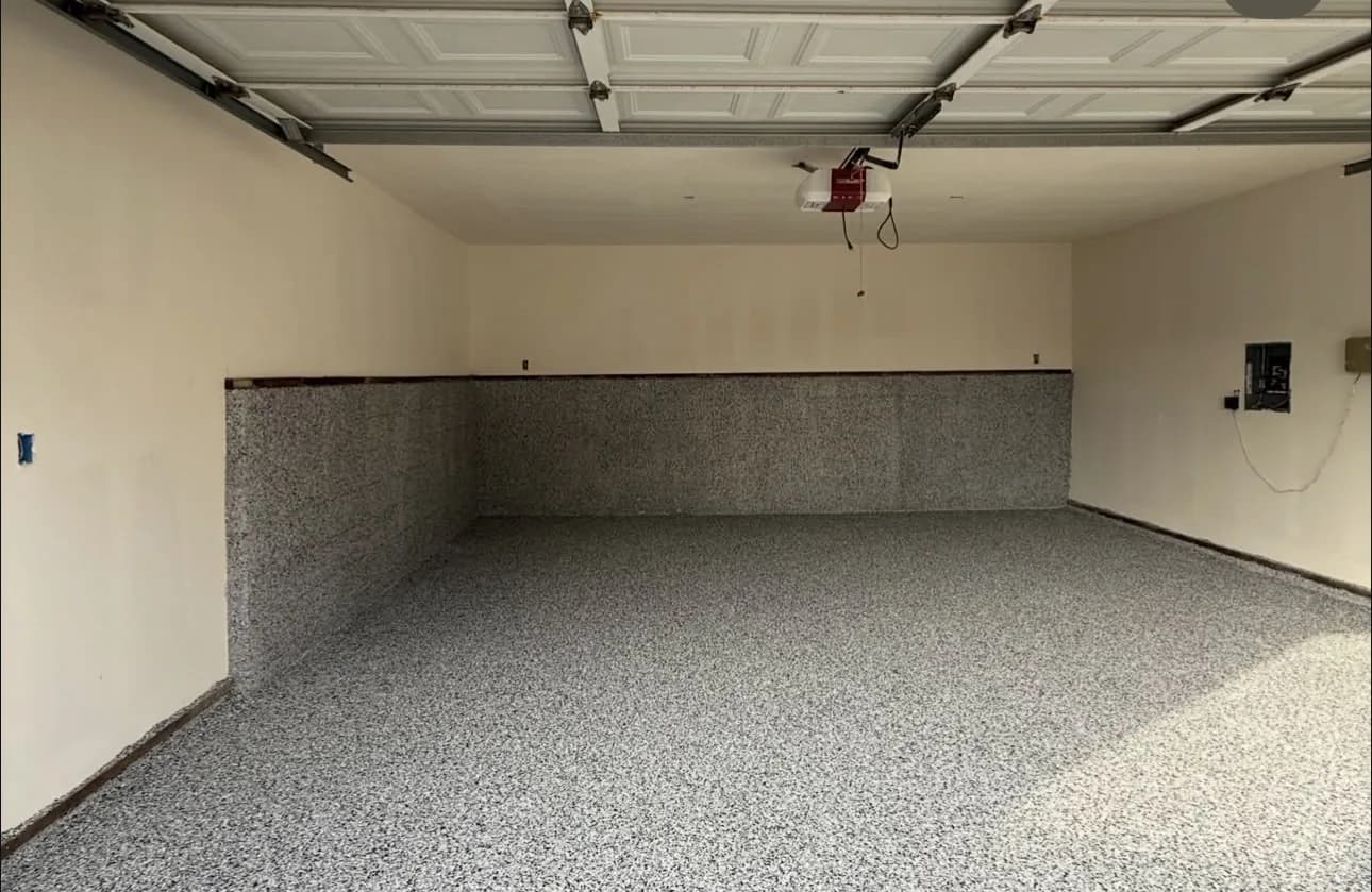 A garage floor in a gray and white flake blend where the coating is carried several inches up the wall as a continuous base rather than stopping at the floor line