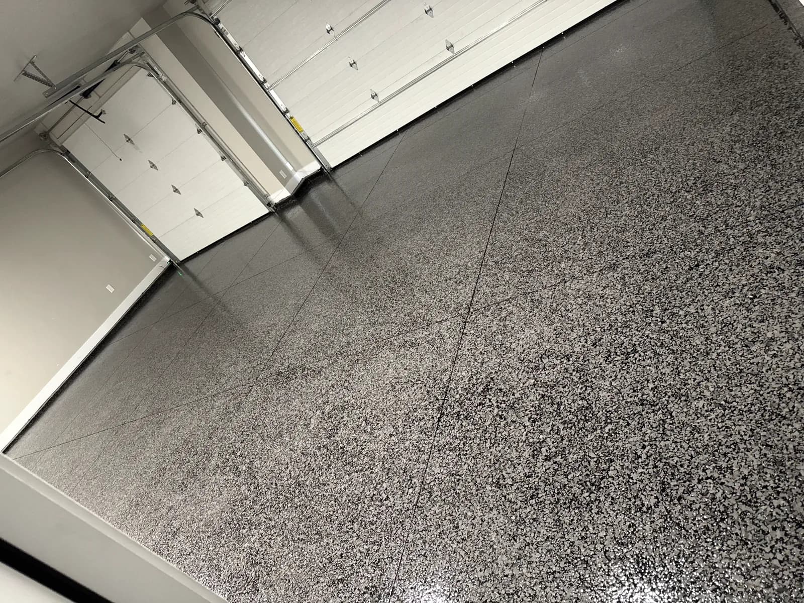 A gray and white flake garage floor photographed from above at an angle, with two white sectional garage doors closed at the top of the frame