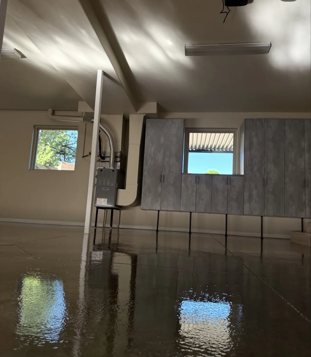 A garage slab still wet after washing, the windows, ceiling and wall cabinets above reflected in the standing water on its surface