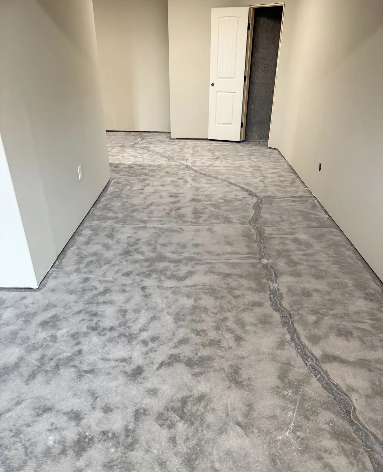 A bare interior concrete slab before work, mottled gray and patchy, with a long crack running the length of it toward an open doorway