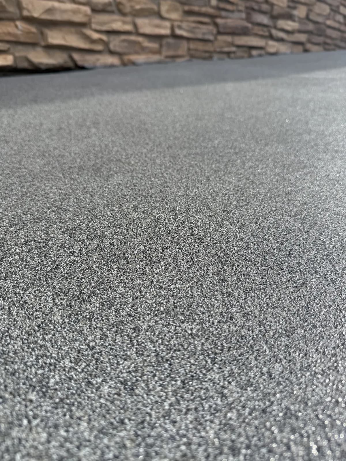 A close view of a fine gray and white speckled porch coating meeting a stacked stone wall at the back of the frame