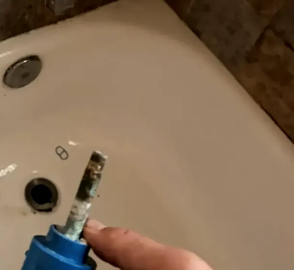 A shower valve cartridge held up after removal, its stem crusted with mineral scale