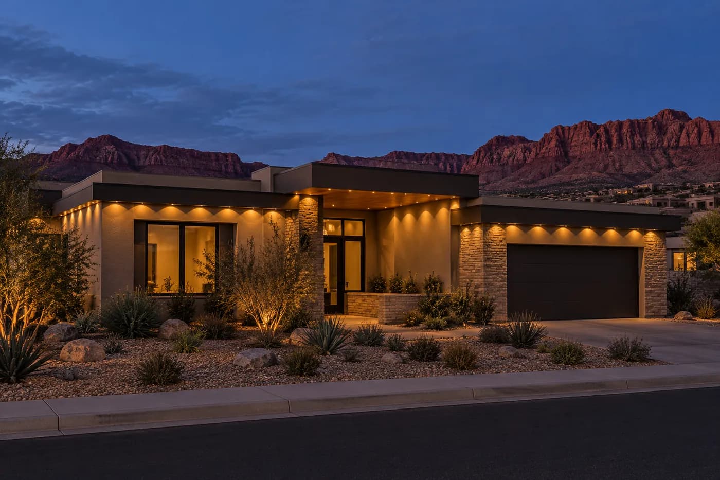 A single-story desert-modern house with flat roof lines and a deep overhang over the entry, every overhang lit in soft gold, red cliffs behind.