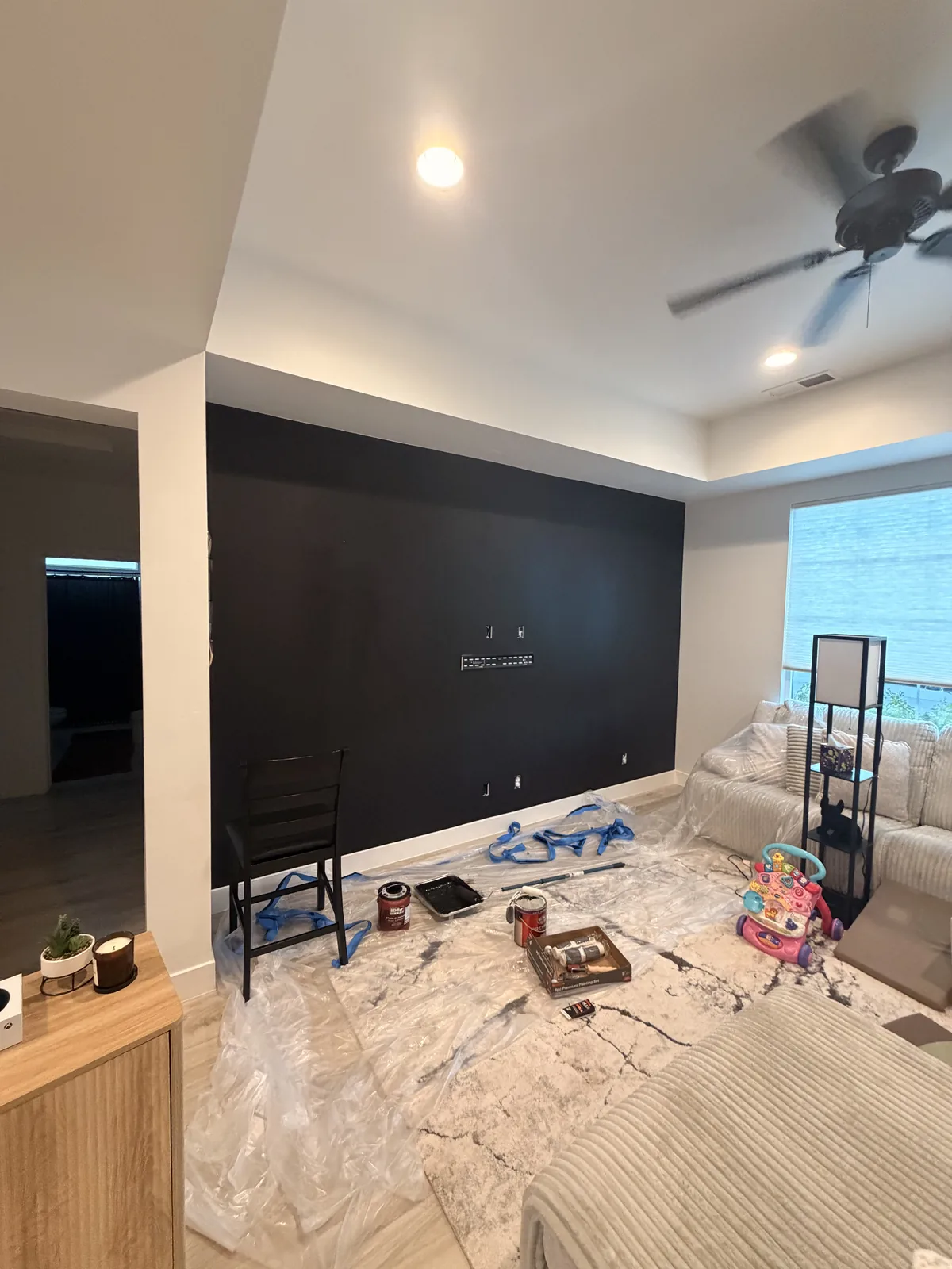 The wall finished in near-black with the drop cloths still down and paint cans and a chair standing on them