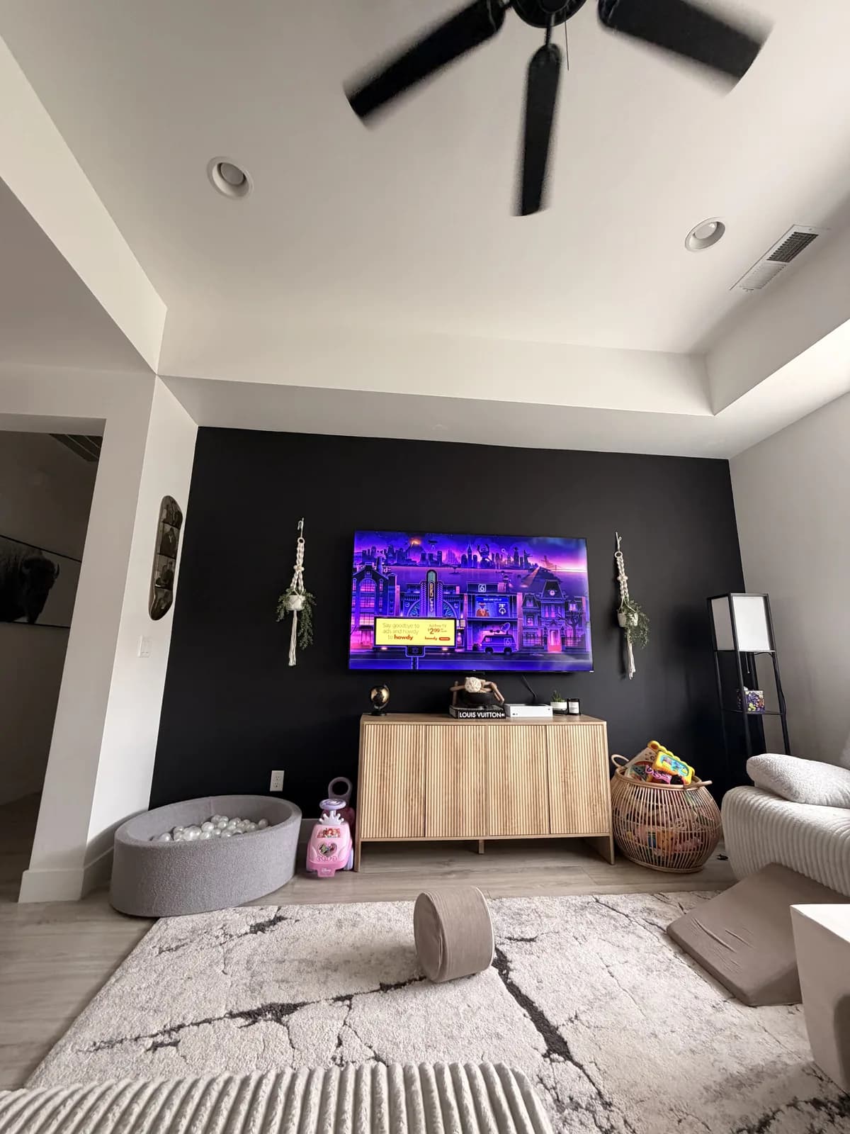 The finished dark wall with the television remounted and switched on, a console beneath it and plants either side