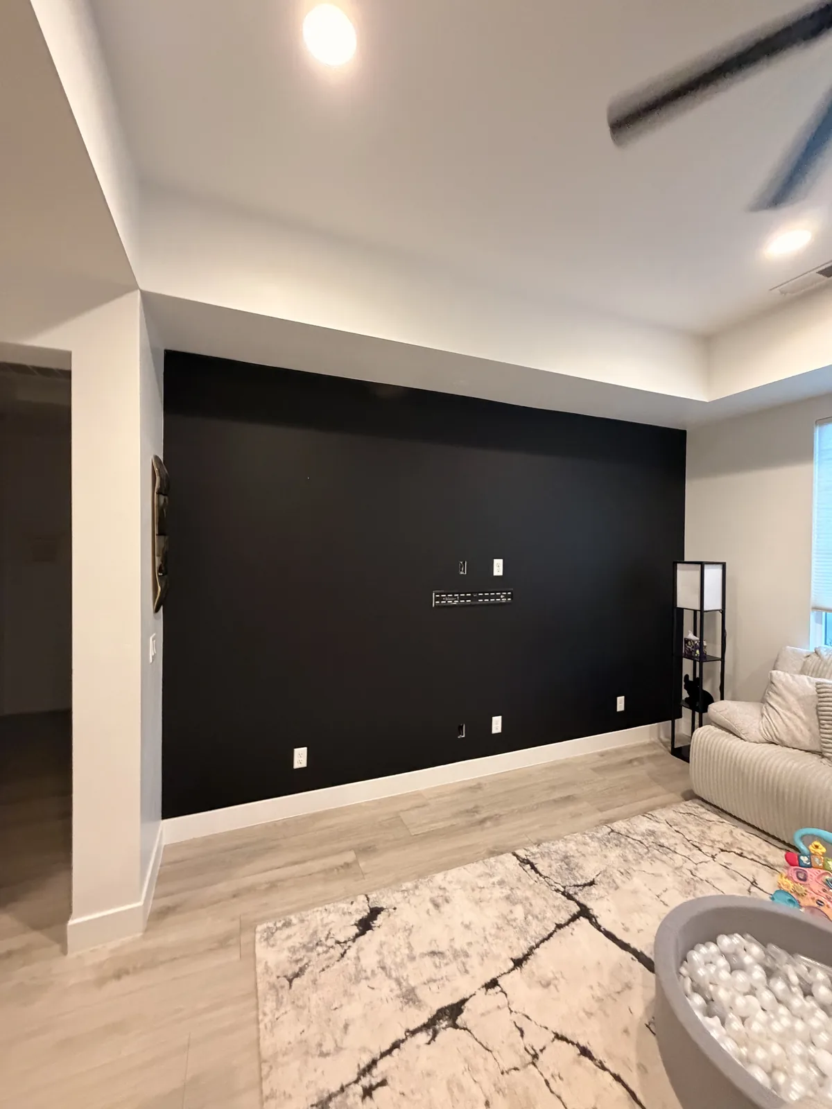 The finished near-black accent wall with the room put back: rug down, furniture returned, and light wood flooring running up to it