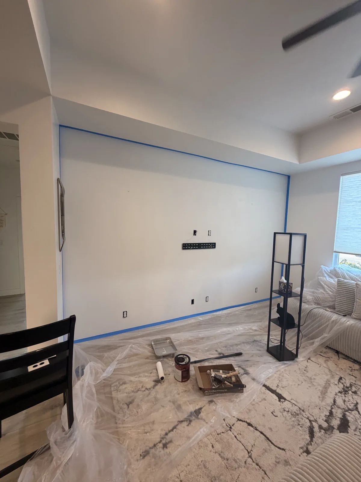 The same room with the furniture pulled back and covered, the floor sheeted, and blue tape run along the edges of the wall to be painted