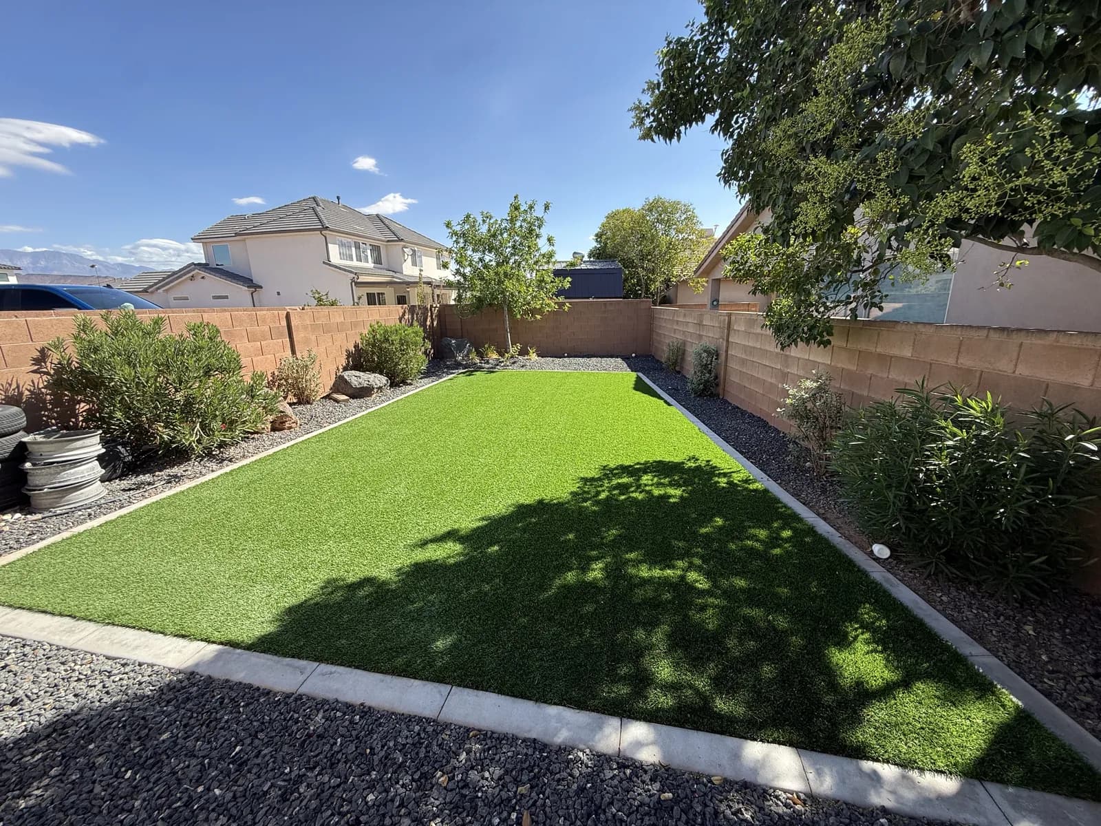A walled back yard with artificial turf edged in concrete, gravel borders and the mountains beyond