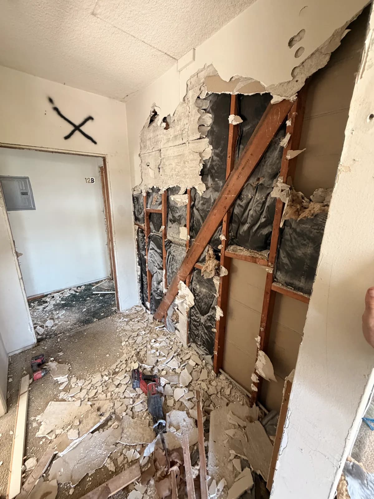A wall opened during demolition, showing the framing and the old pipework inside it
