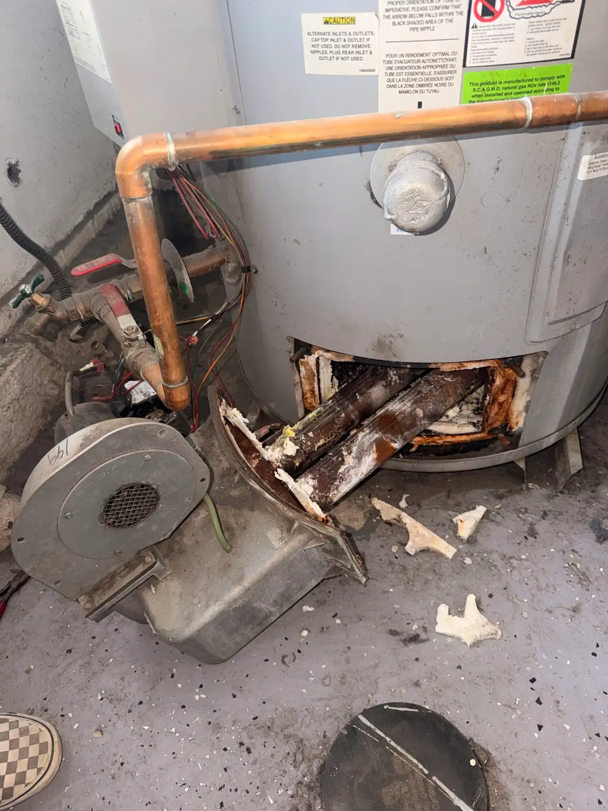 A corroded old water heater pulled out during a replacement, showing years of scale and rust