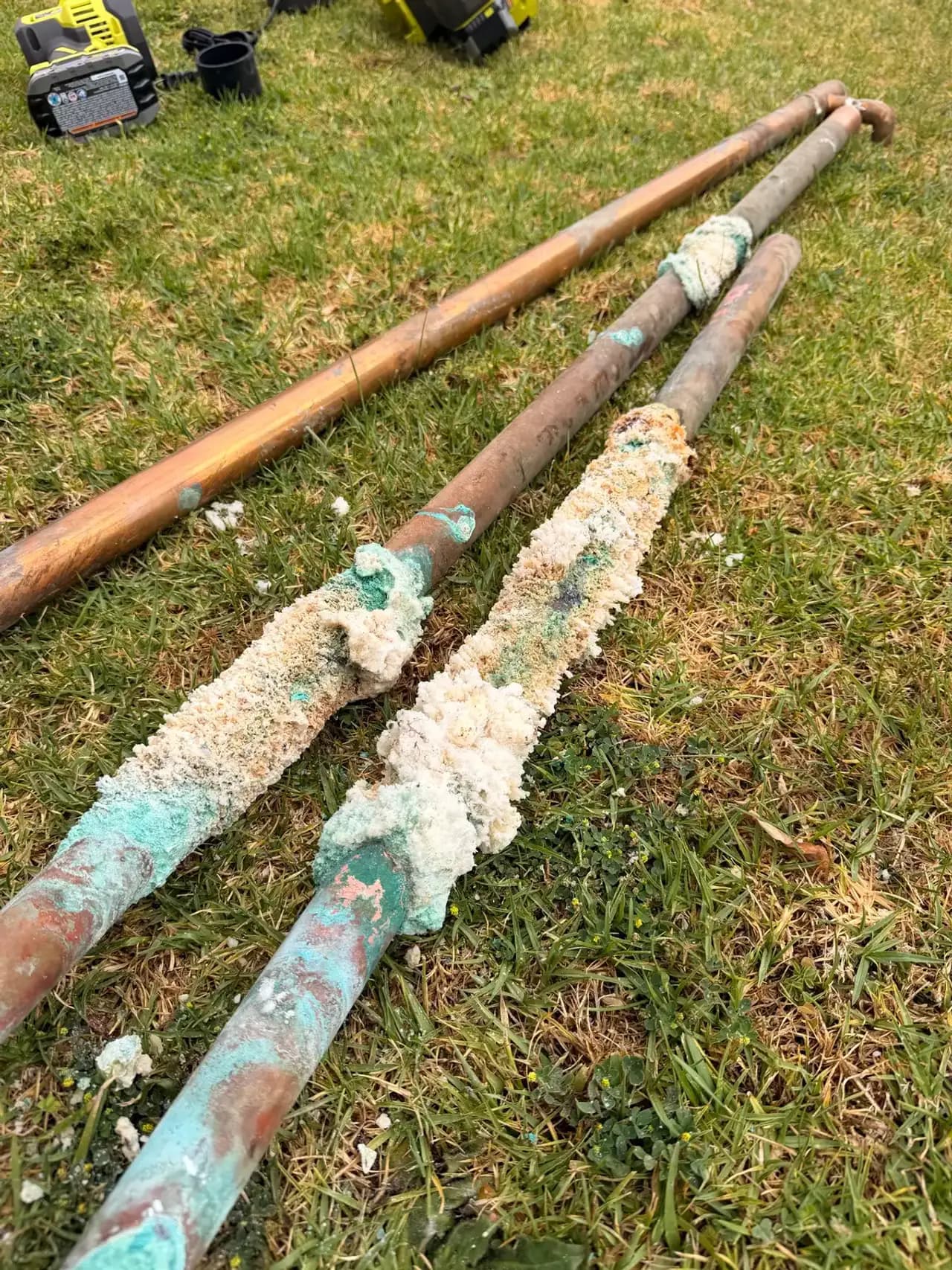 Severely corroded copper water main lines removed from a house during a repipe, with heavy green verdigris and mineral buildup at the leak points
