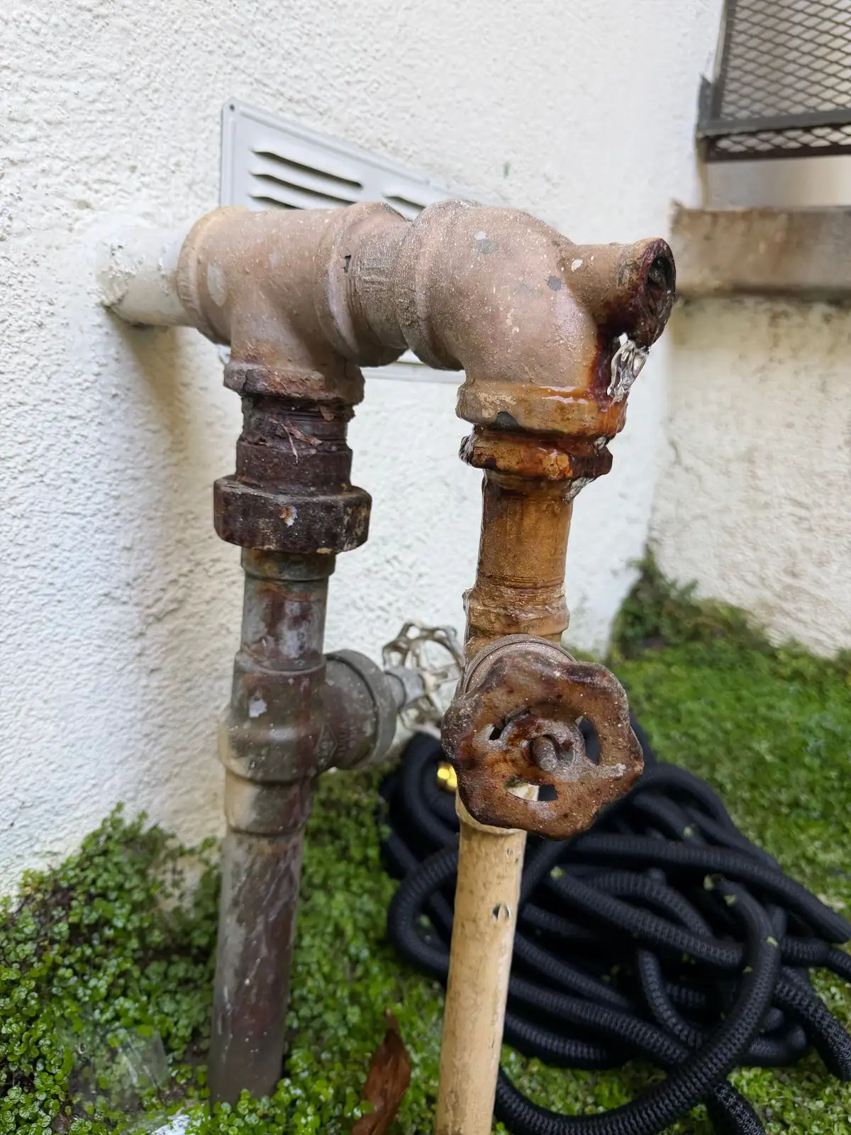 A heavily corroded galvanised water supply riser with mineral buildup and active rust at the joint