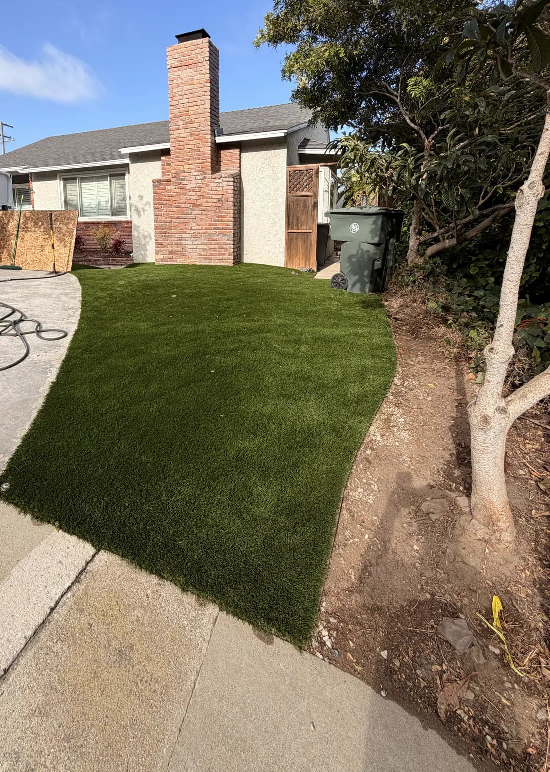 A front yard laid with artificial turf beside a concrete drive, with a bare planted strip along the boundary