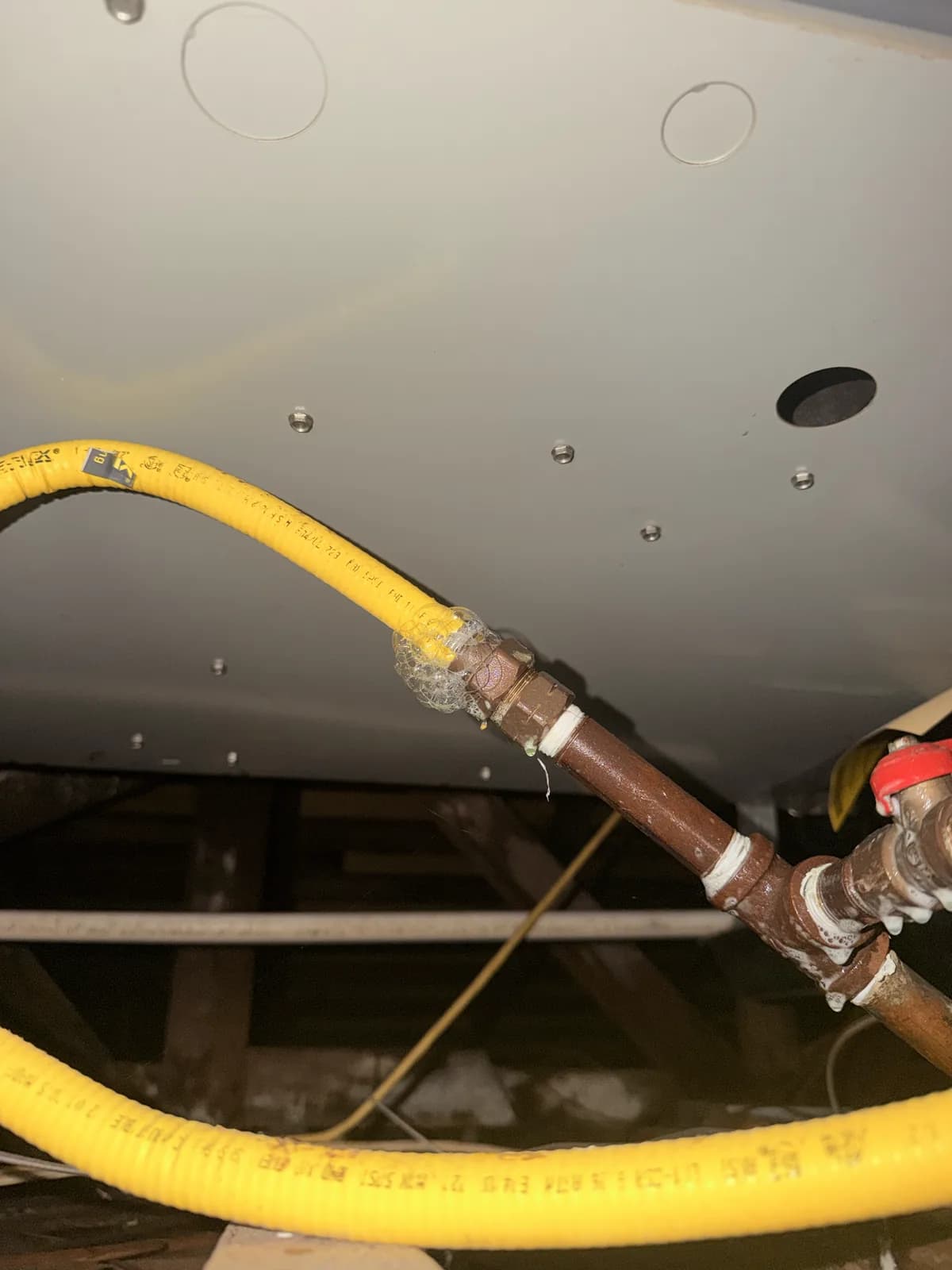 A yellow corrugated gas connector and copper water lines running to the underside of a water heater