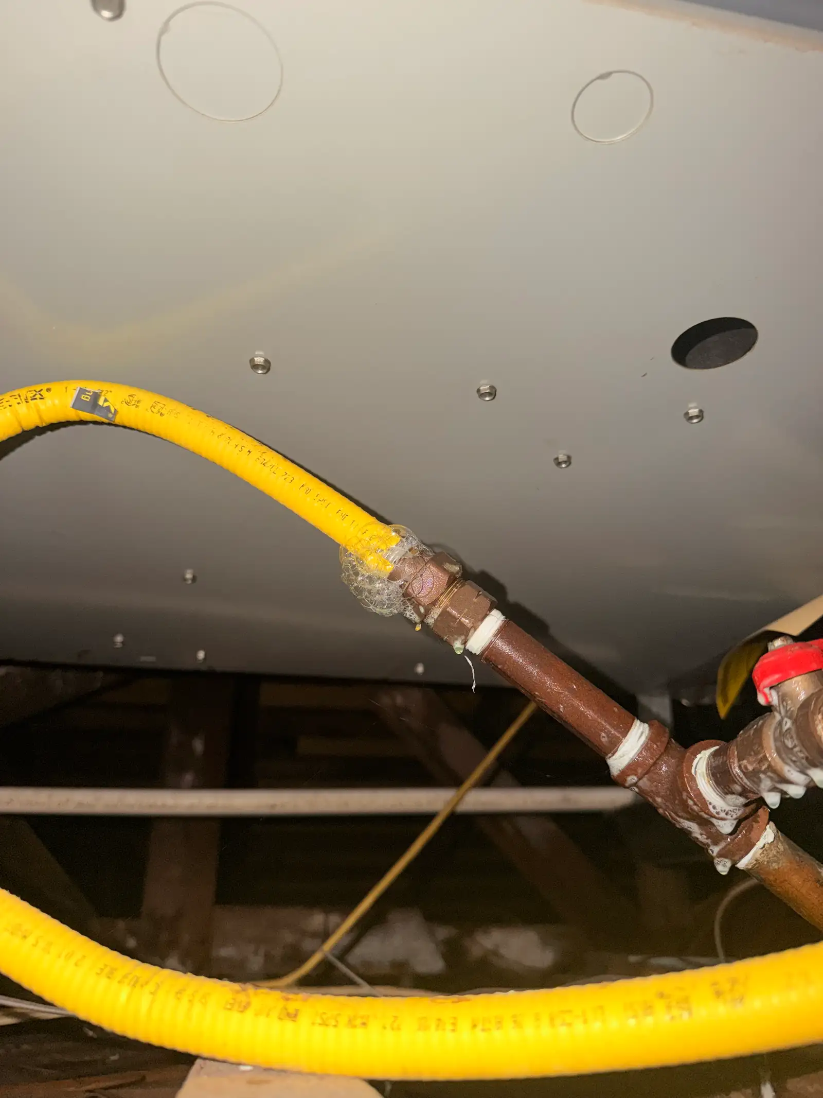 Soap solution bubbling at a threaded gas fitting during a leak test in a crawl space