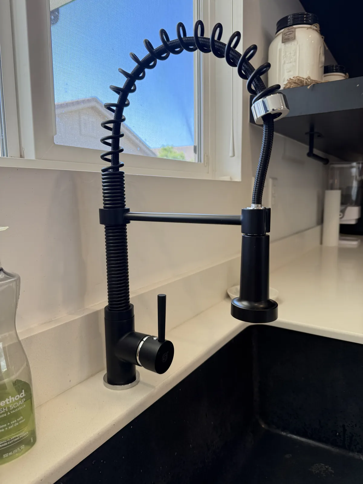 A black spring-neck kitchen faucet with a pull-down sprayer at a white quartz counter over a dark sink
