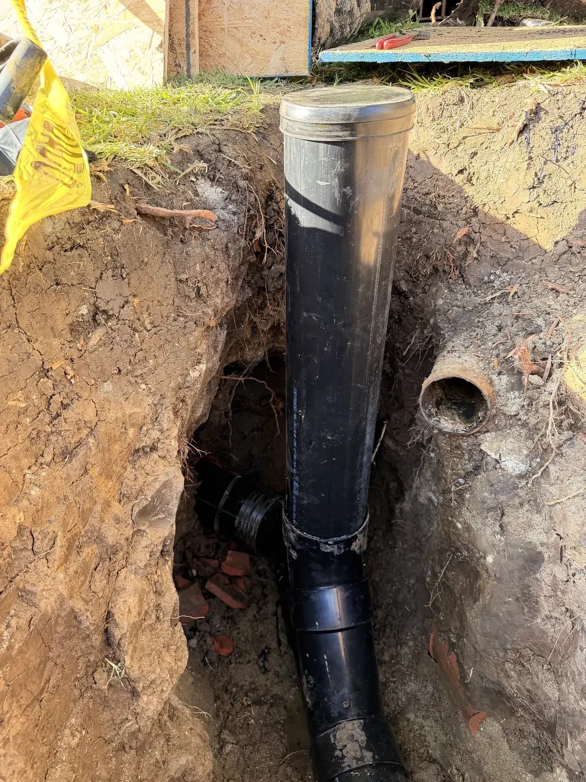 An excavation showing the new sewer pipe standing beside the cut end of the old line