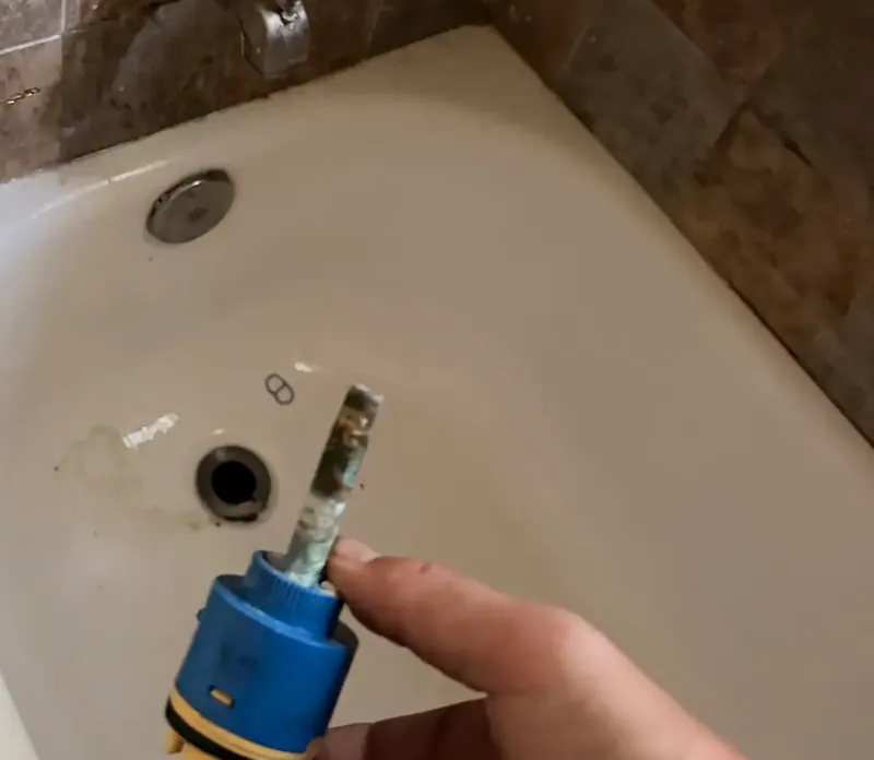 A shower valve cartridge covered in mineral scale, removed from the wall
