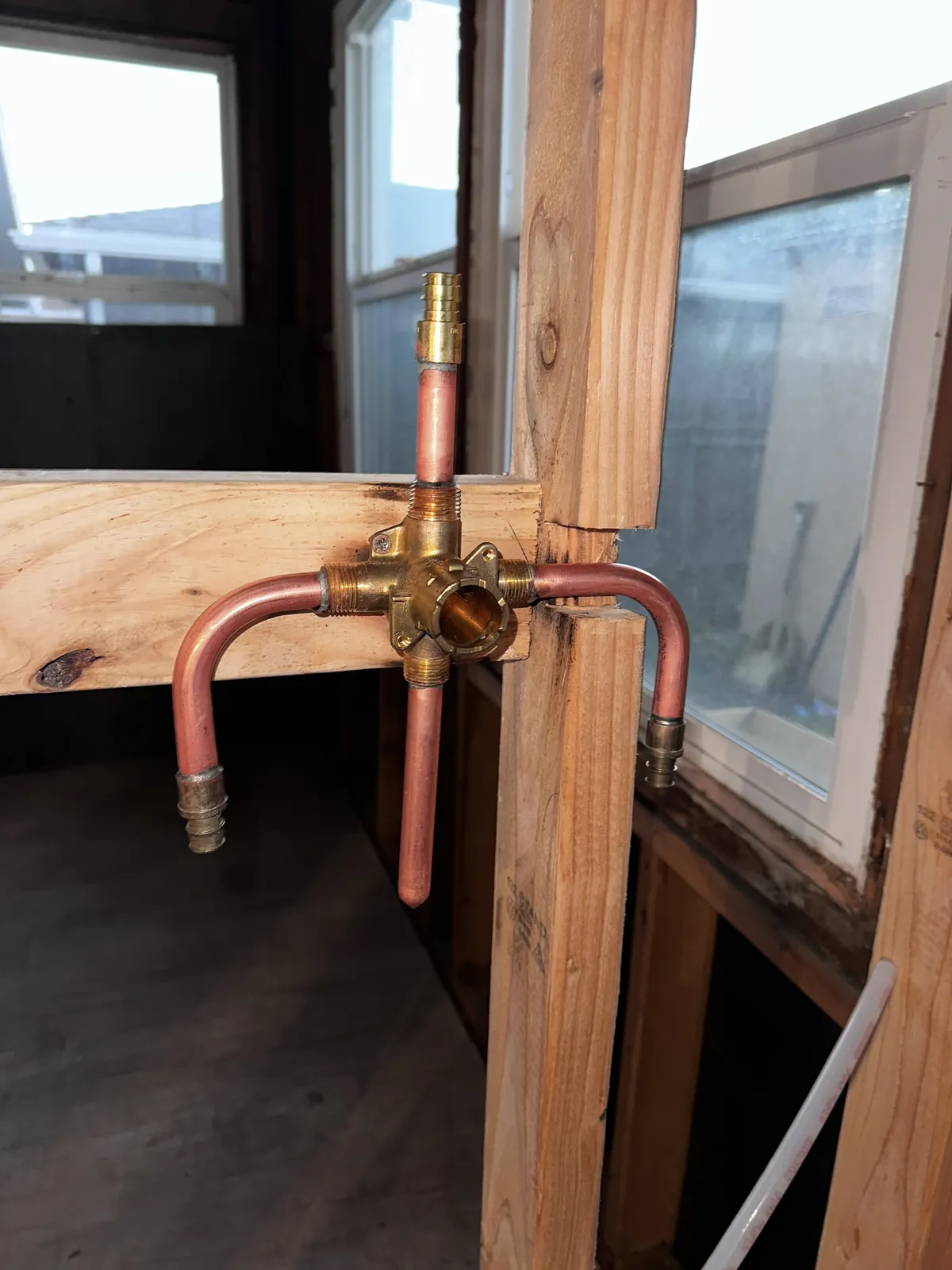 A shower mixing valve roughed in on copper between two studs, braced to a block, with stub-outs above for the head and below for the spout