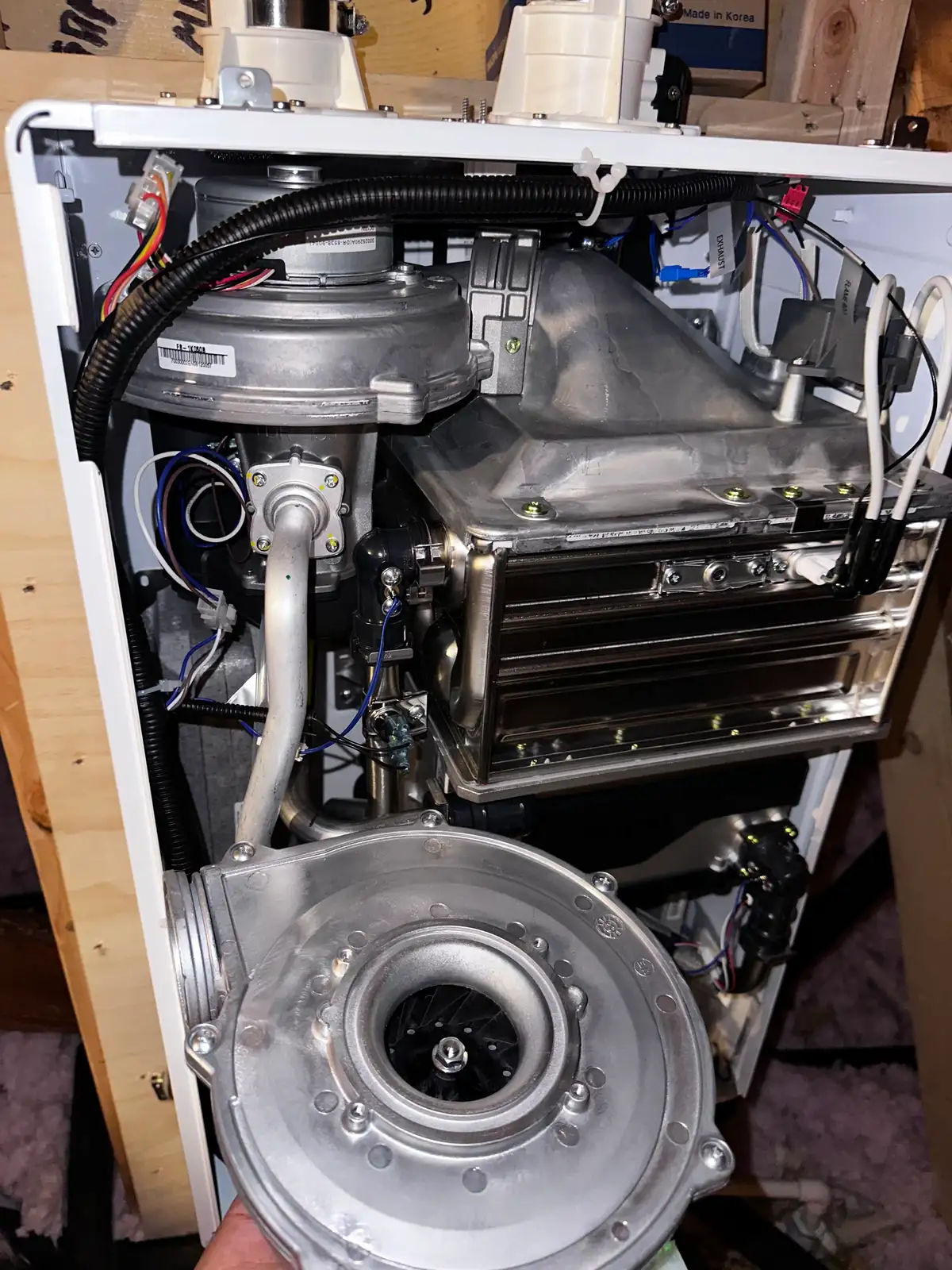 A wall-mounted condensing tankless water heater opened for service, showing the copper gas and water connections and the plastic venting