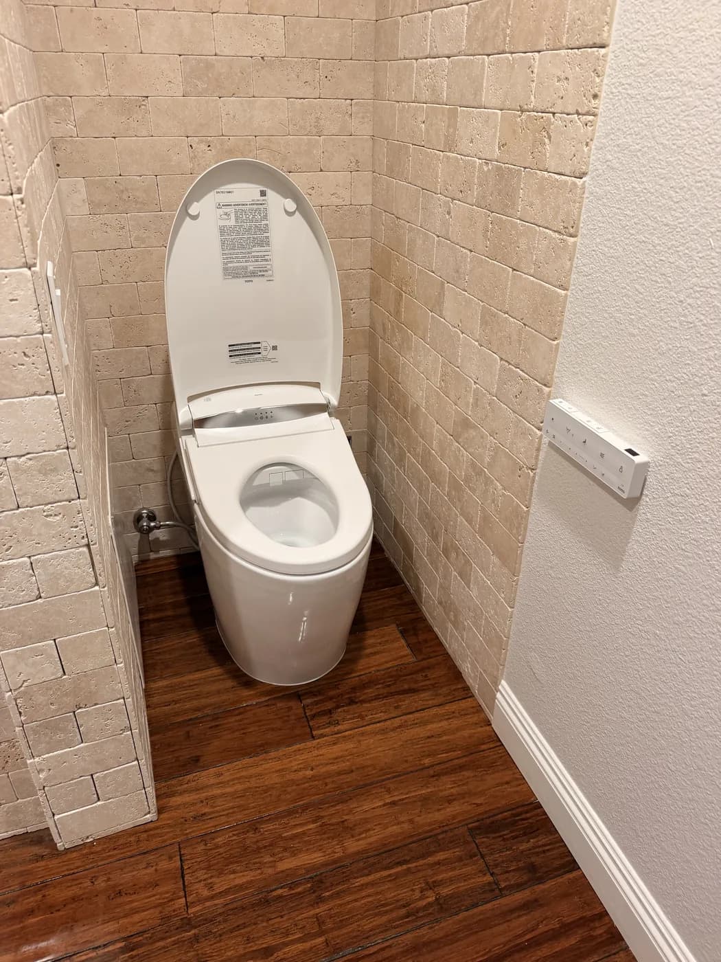 The same toilet with the lid raised, showing a washlet-style seat with a control panel on its side