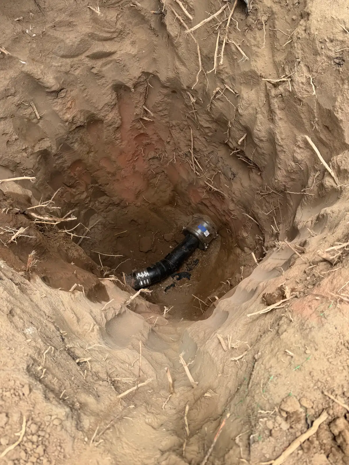 A single compact pit opened in the ground exposing the old sewer pipe, with no trench beyond it