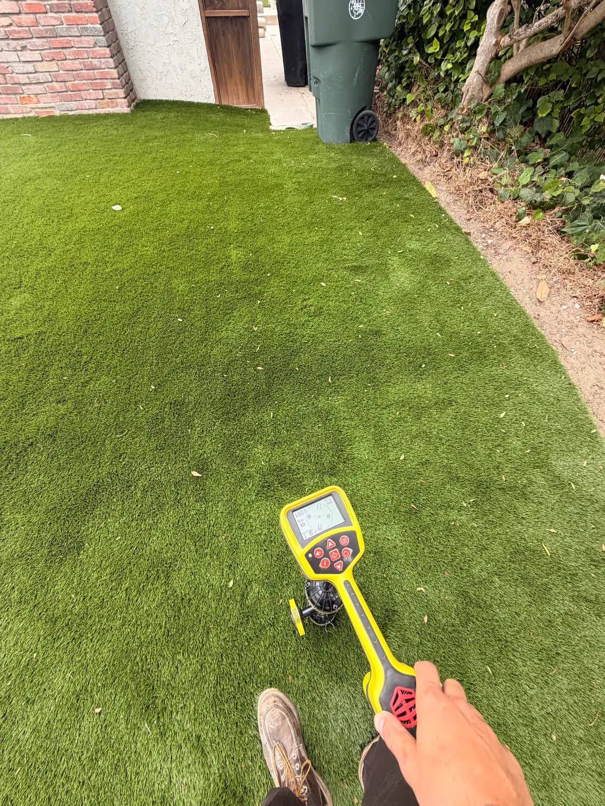 A technician using a locator to find and mark the sewer line across a front lawn before work starts