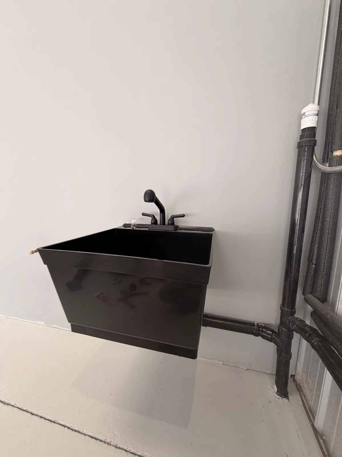 A wall-mounted utility sink installed with its trap and supply pipework visible below