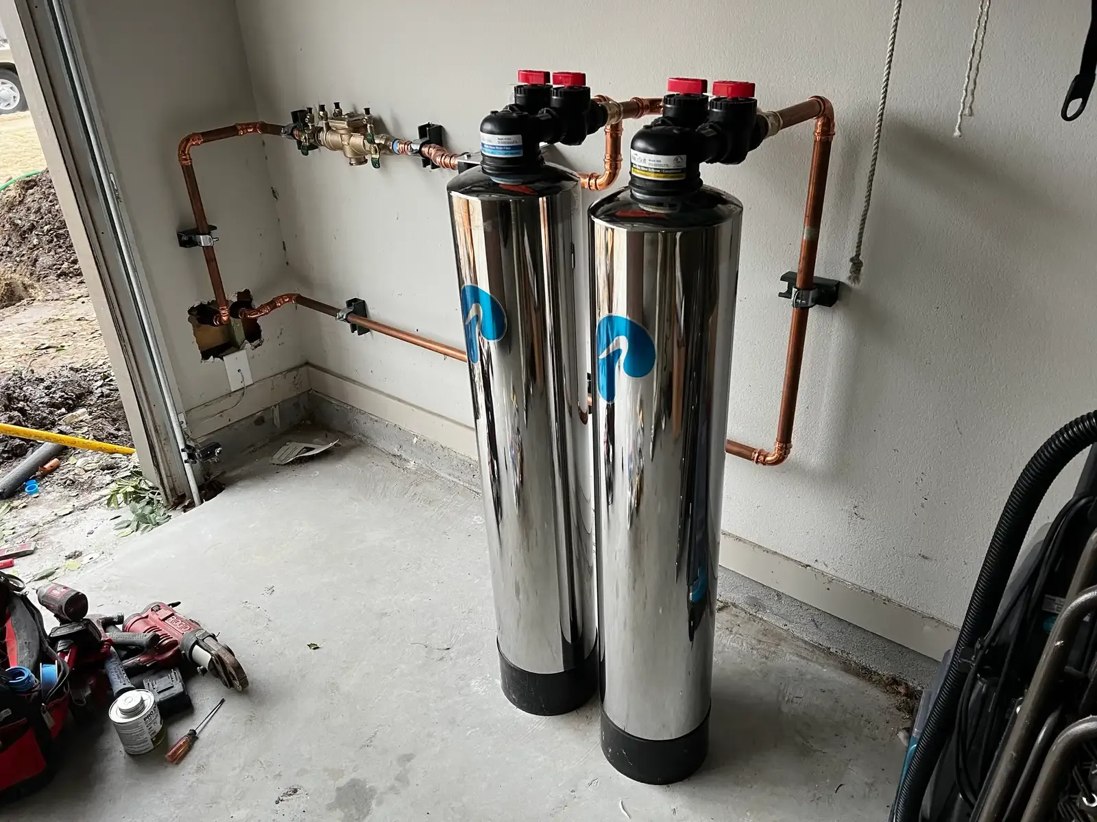 A whole-house filtration and softening system plumbed into the main line on a garage wall