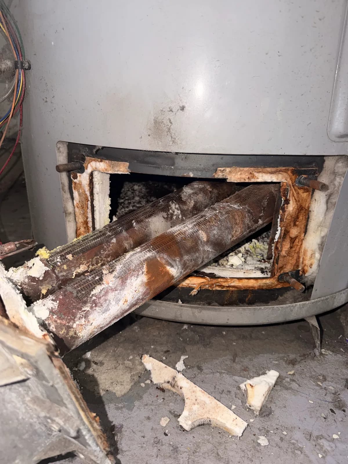 The open base of an old water heater showing a badly corroded burner assembly and rusted debris