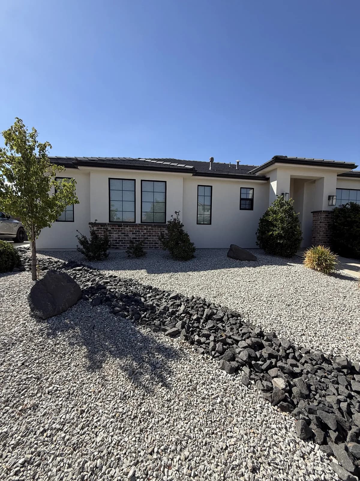 A converted front yard in pale gravel with a dry creek of dark rock, young trees and desert shrubs against a white stucco house