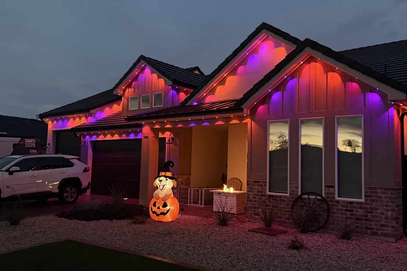 A single-story house at dusk with lights along every roofline, throwing orange and purple scallops of light down the walls.